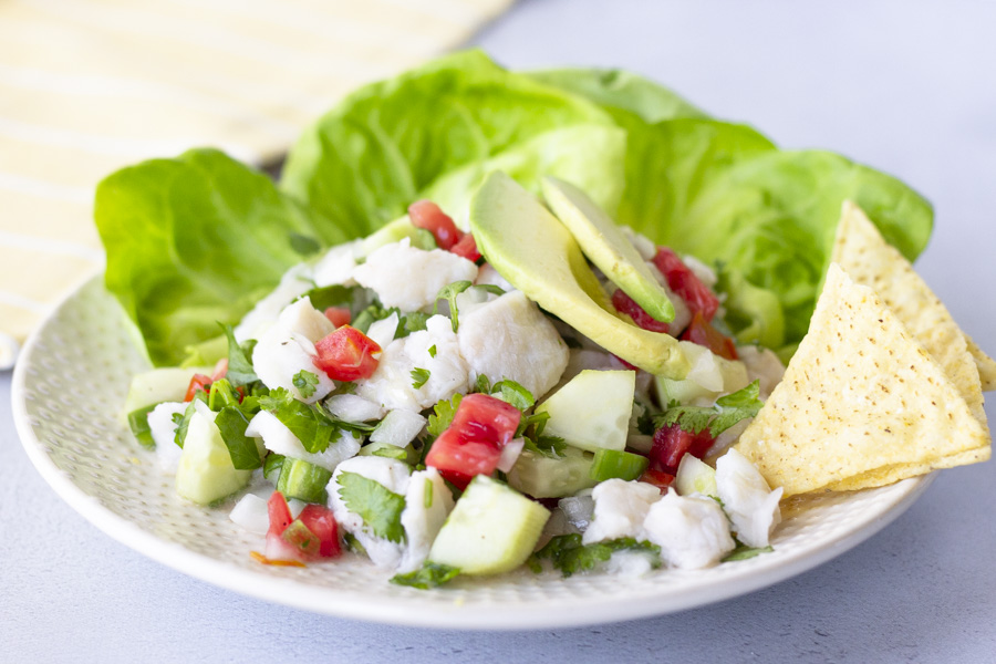 Horizontal view of Fish ceviche on a plate with lettuce leaves, topped with avocado, and chips on the side.