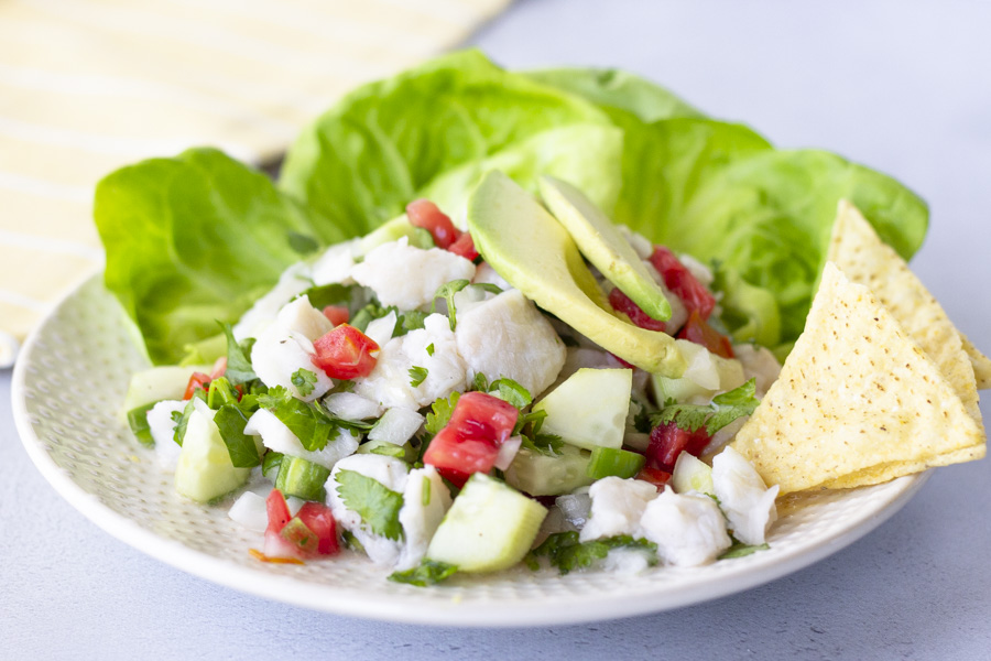 Vista orizzontale di ceviche di pesce su un piatto con foglie di lattuga, condita con avocado, e patatine sul lato.