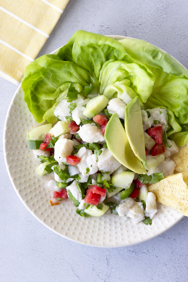 Overhead view of fish ceviche on a plate with lettuce leaves and topped with avocado.