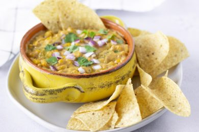 Horizontal view of dairy free elote dip in a yellow bowl with tortilla chips on the side.