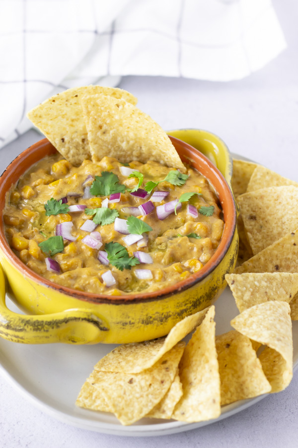 Mexican Street Corn Dip in a yellow bowl topped with red onions, cilantro, and tortilla chips.