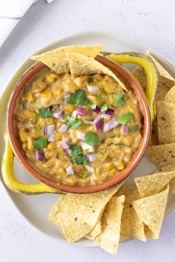Overhead view of Elote Dip in a yellow bowl topped with red onions, cilantro, and tortilla chips.