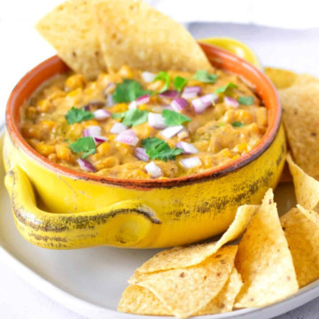 Yellow dish holding elote dip with chips on the side.