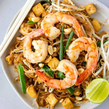 Overhead view of pad thai with shrimp on white plate with chopsticks on the side.