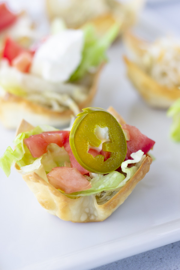 Up close view of taco wonton topped with lettuce, tomato, and a jalapeno.