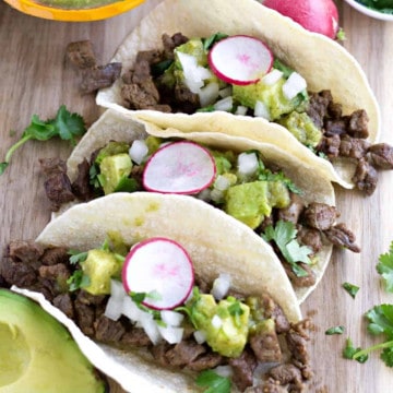 Three carne asada steak tacos on a board.