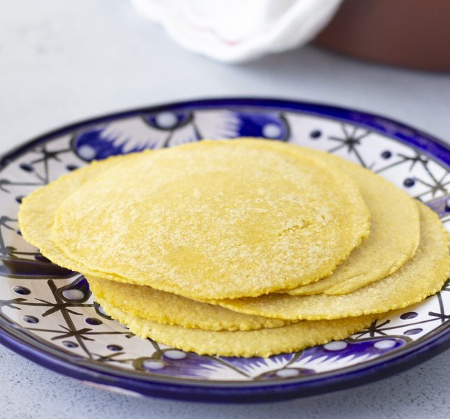 Horizontal view of yellow corn tortillas stacked on a blue plate.