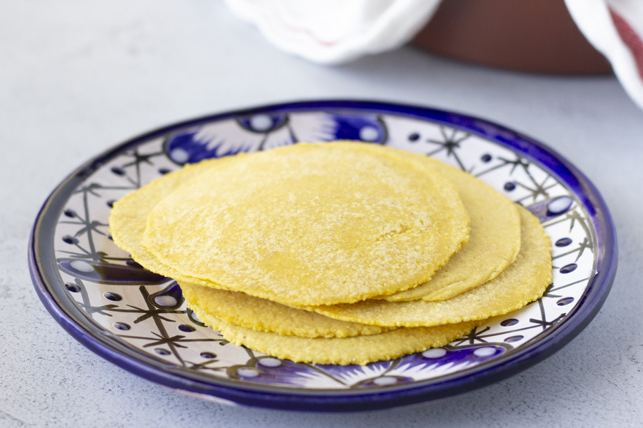 Horizontal view of yellow corn tortillas stacked on a blue plate.