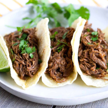 Up close view of 3 shredded beef tacos on a plate.