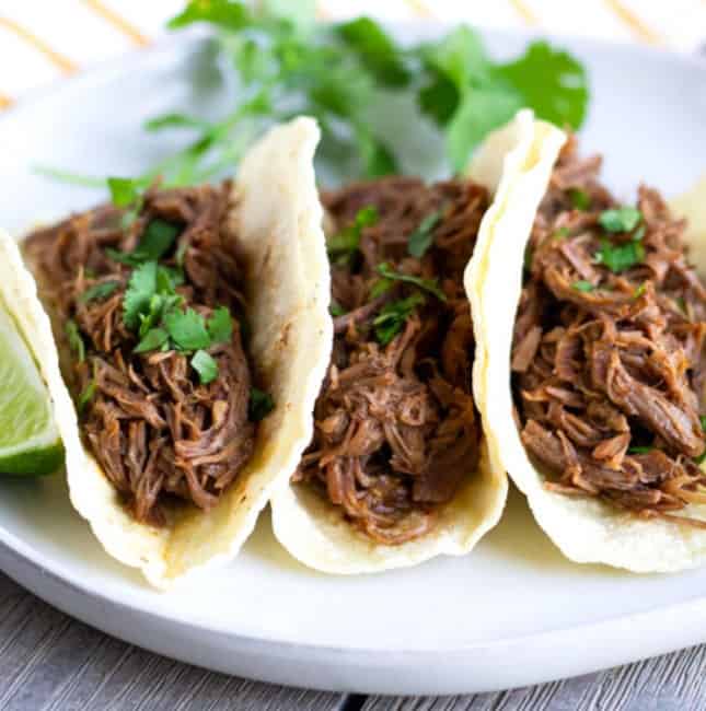 Up close view of 3 shredded beef tacos on a plate.