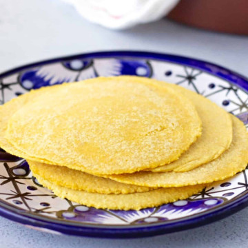 Yellow corn tortillas stacked on a blue plate.