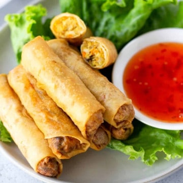 Fried Spring rolls stacked on a plate of lettuce and a side of sweet chili dipping sauce.