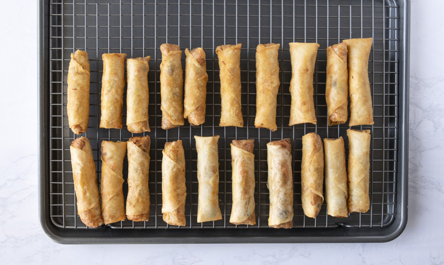 Cooked spring rolls cooling off on a wire baking rack.