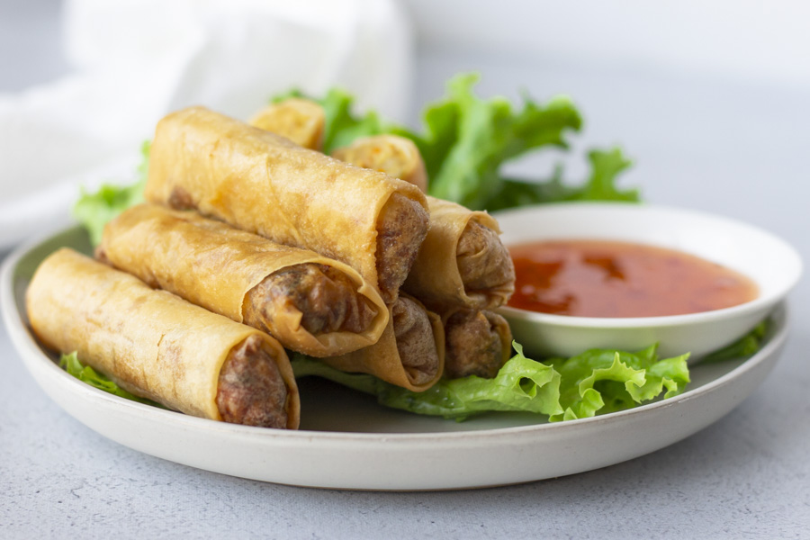 Crispy rolls on a bed of lettuce on a plate with a side of sweet chili dipping sauce.