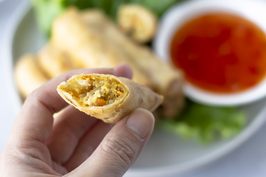 Hand holding a half spring roll to show filling inside.