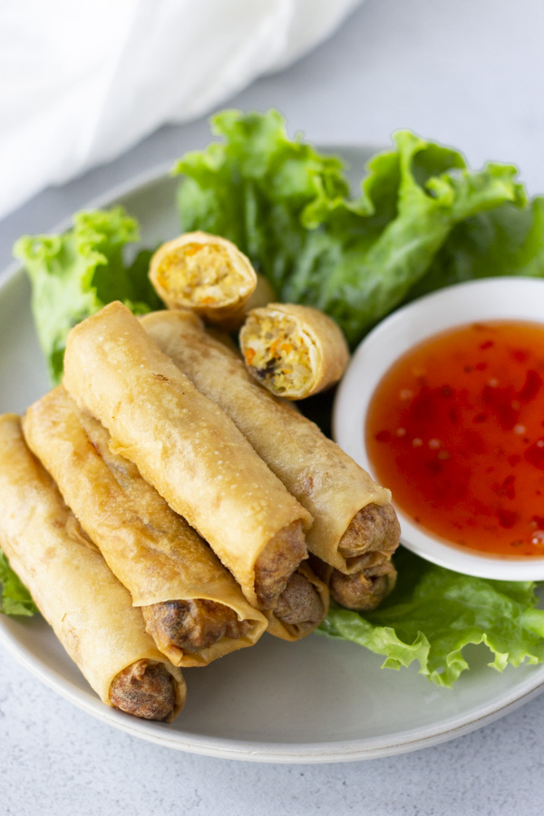 Spring Rolls on top of a bed of lettuce on a plate with a side of sweet chili dipping sauce.