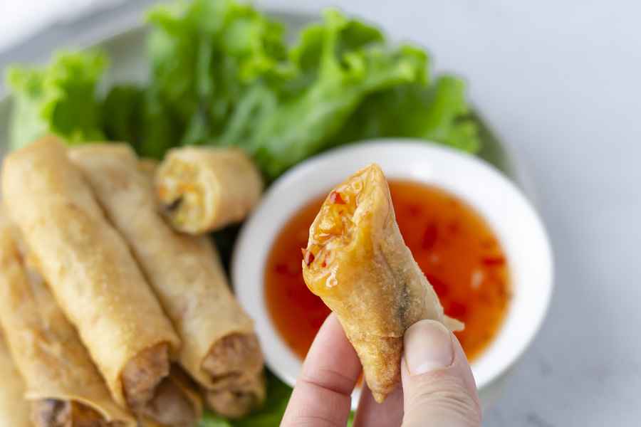 Hand holding half of a spring roll that was dipped in sweet chili sauce.