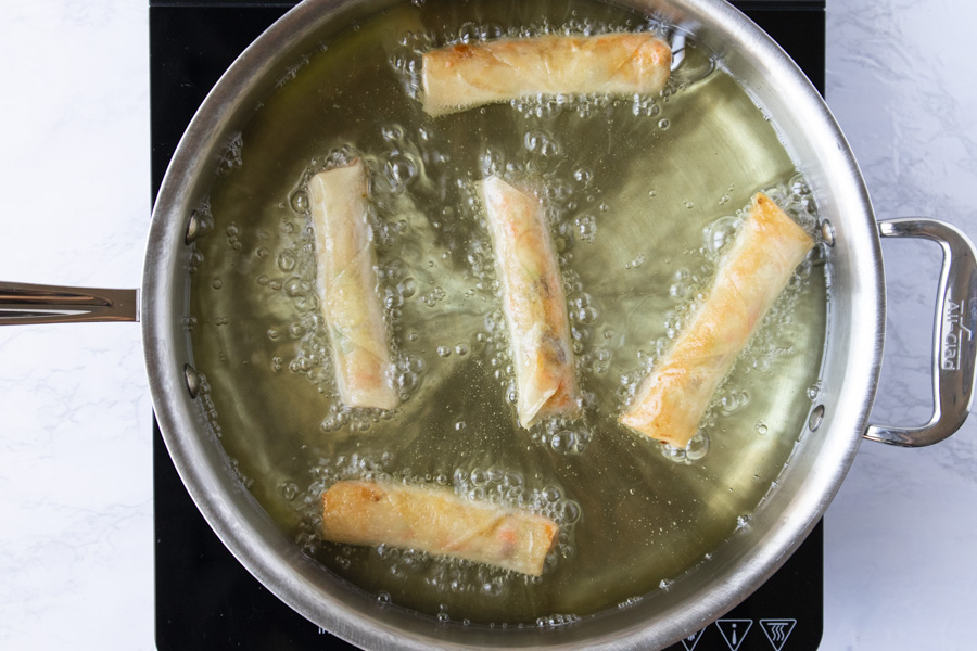 Spring rolls being fried in a pot of oil.