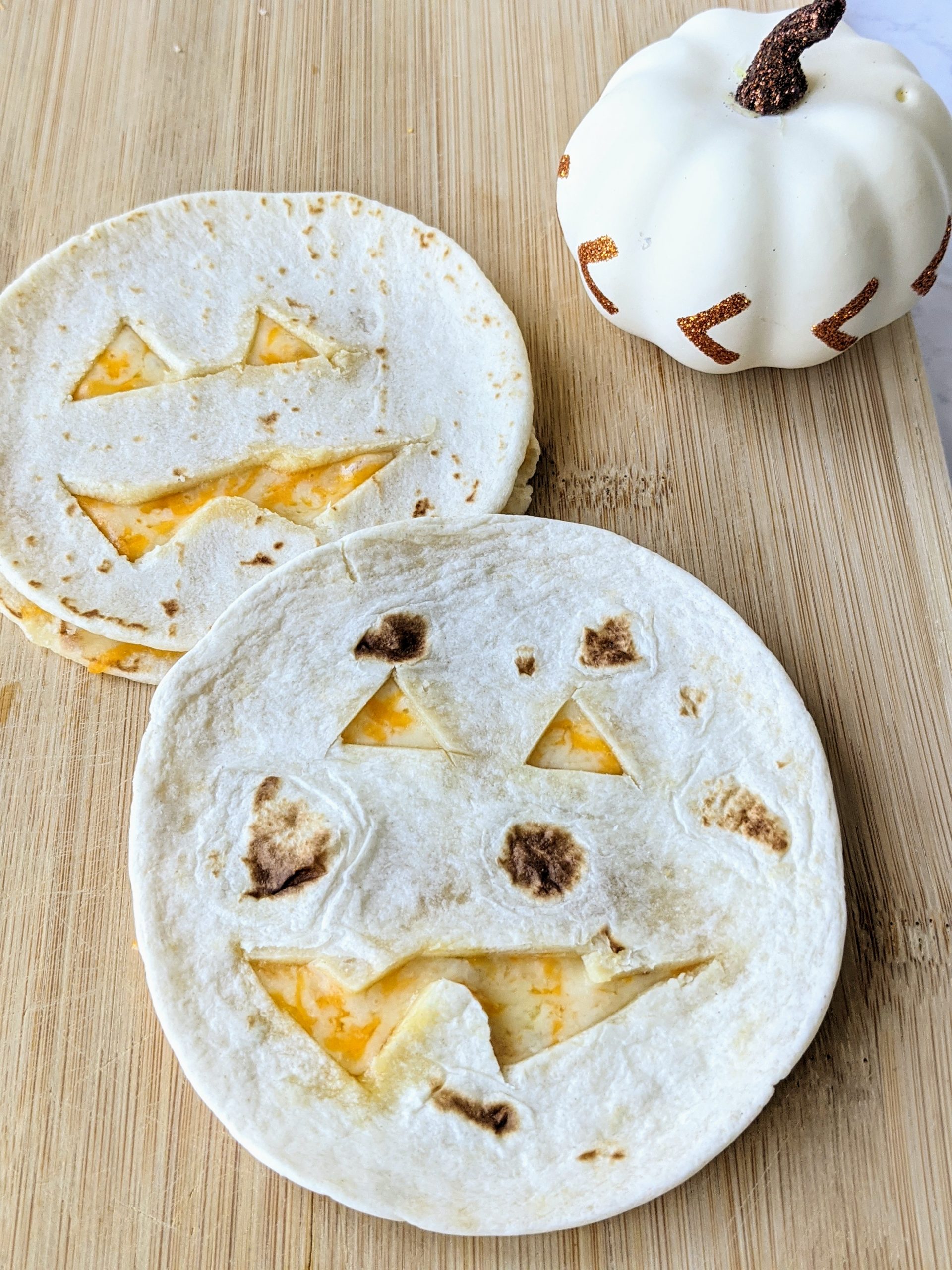 Two Quesadillas cut out like Jack o lanterns on a cutting board.