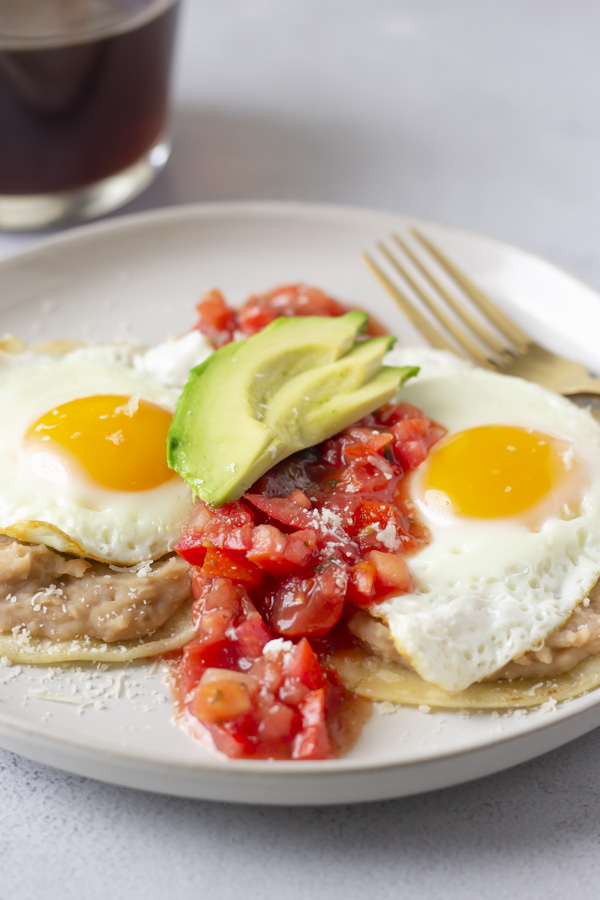 Up close view of dish with salsa down the middle of the 2 eggs and topped with avocado slices.