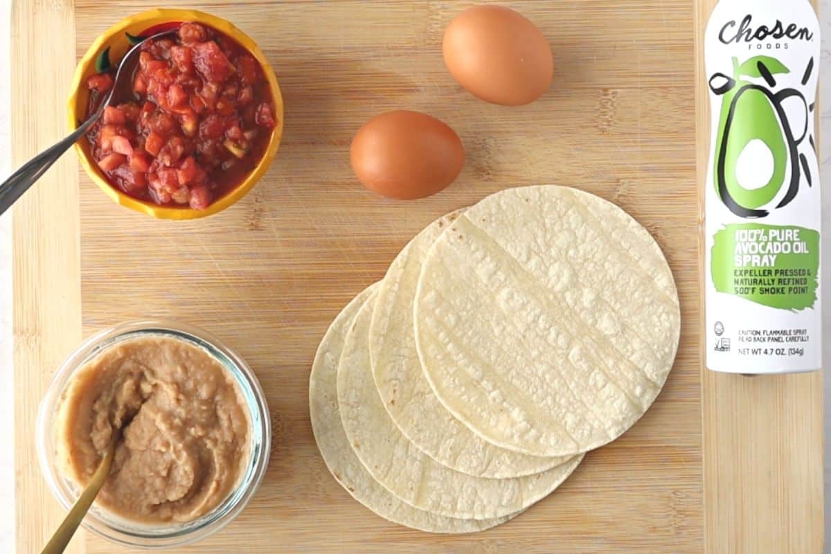 Salsa, beans, tortillas, eggs, and spray oil on a board.