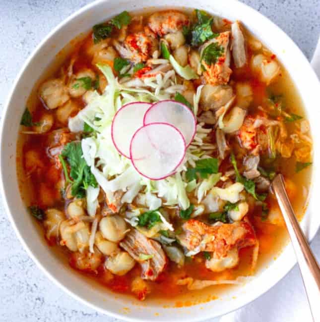 A large white bowl holding the soup and topped with shredded cabbage, cilantro, and thinly sliced radishes.