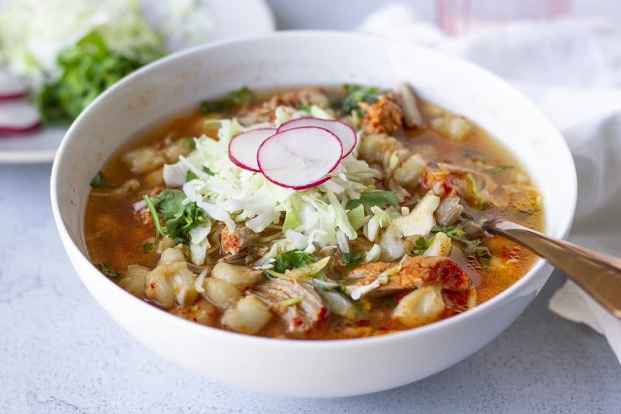 A large white bowl holding the soup and topped with shredded cabbage, cilantro, and thinly sliced radishes.