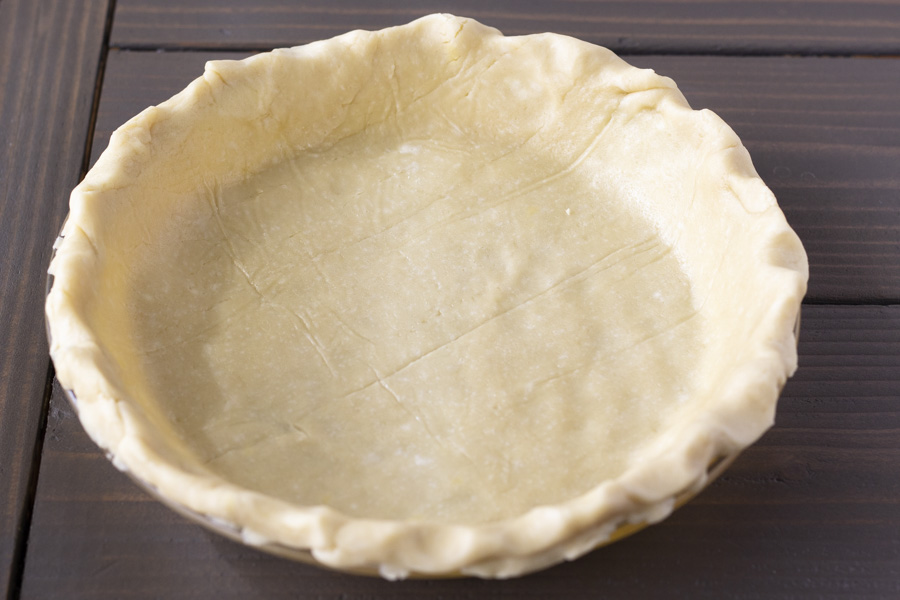 Unbaked pie crust in a glass dish on a wood table.