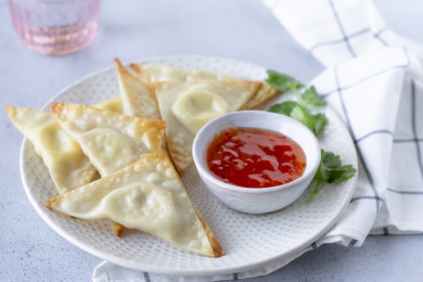 Cream cheese wontons on a plate with other wontons and a side of sweet chili sauce.