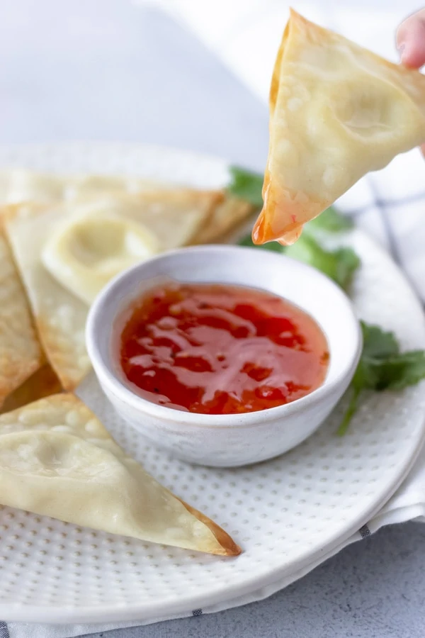 Hand holding a wonton that was dipped in sweet chili sauce.