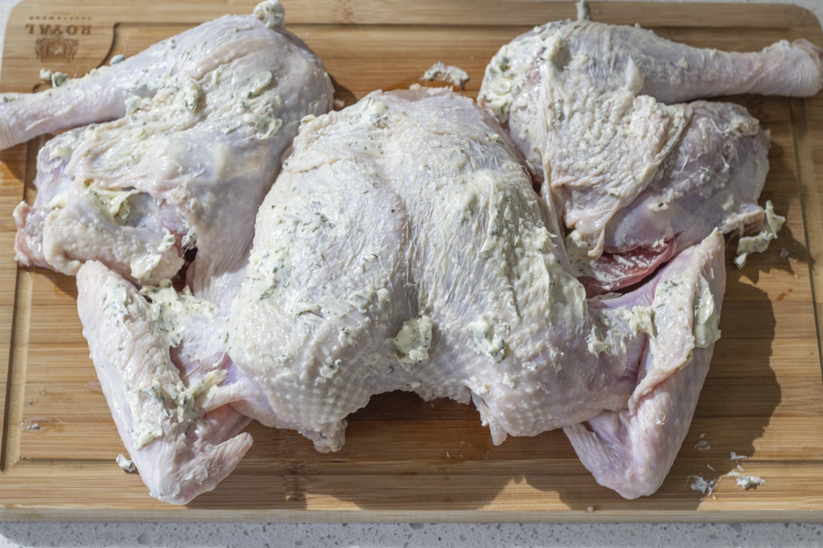 Overhead view of raw turkey covered in herb butter on a wood cutting board.