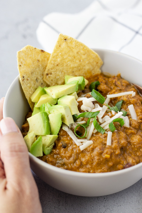 Hand holding the bowl with chili inside.