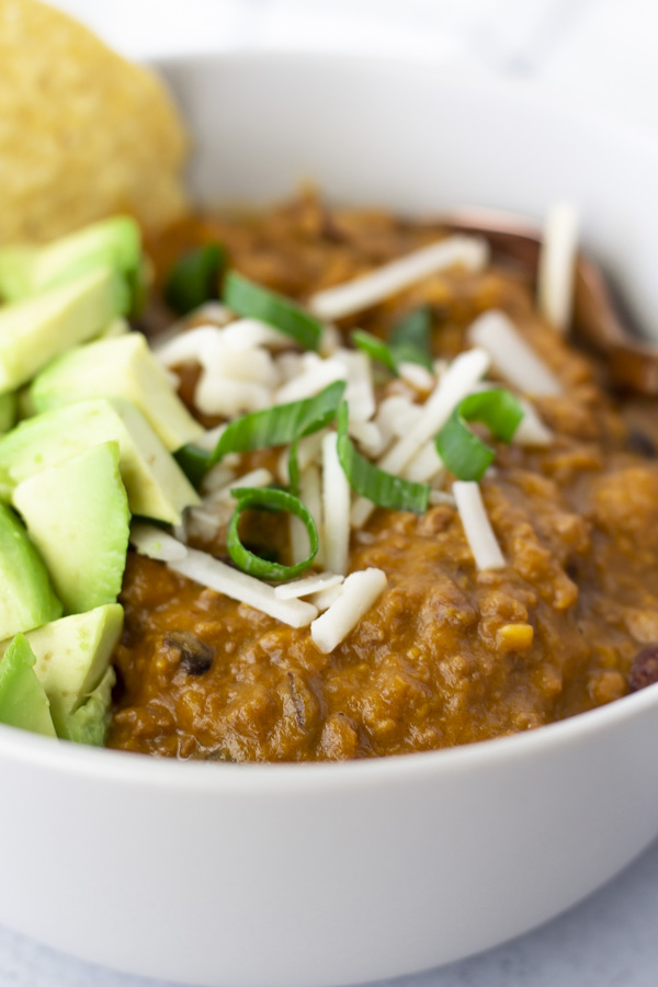 Up close view of Chili in a bowl topped with cheese, onions and diced avocado.