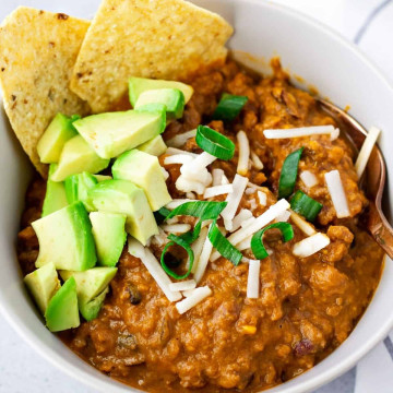 Chili in a bowl topped with cheese, avocado, and tortilla chips.