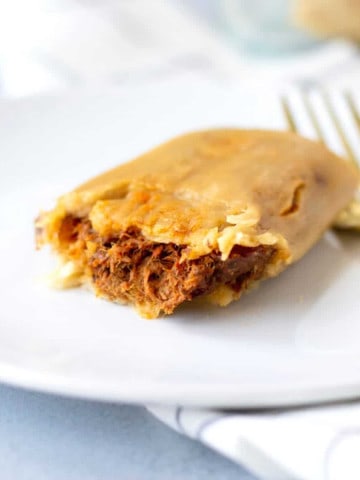 Up close view of a single beef tamale on a white plate with a gold fork on the side.