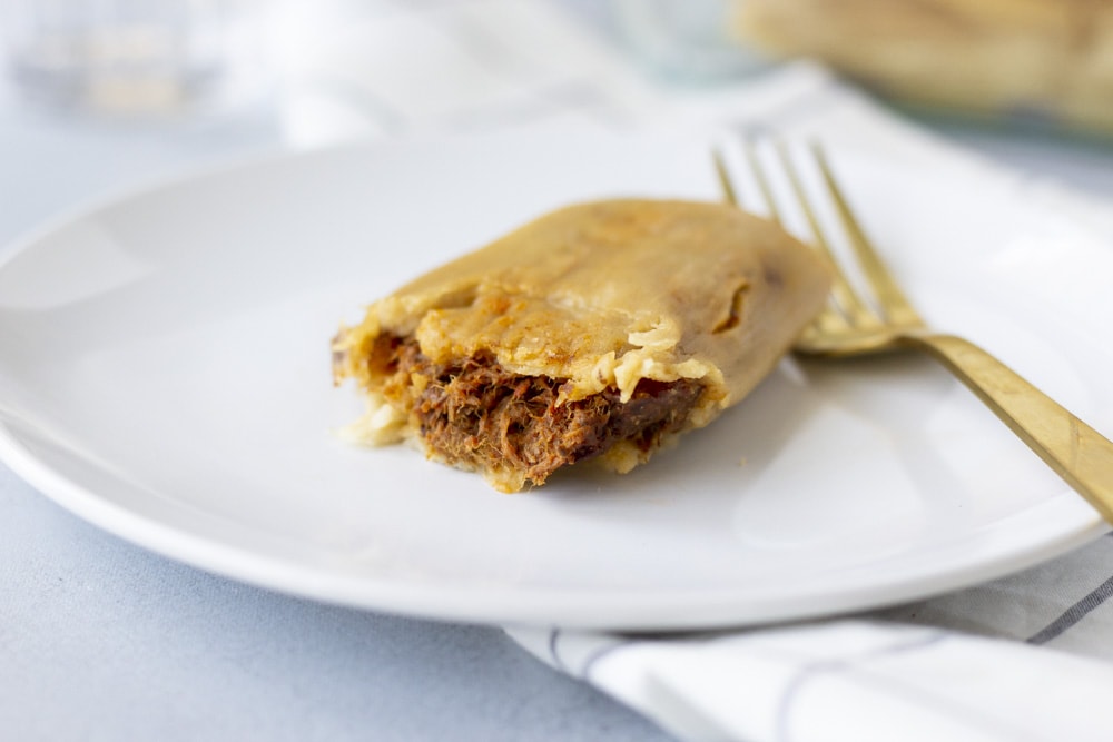 Landscape view of tamale on a white plate with a gold fork and view of been filling inside.
