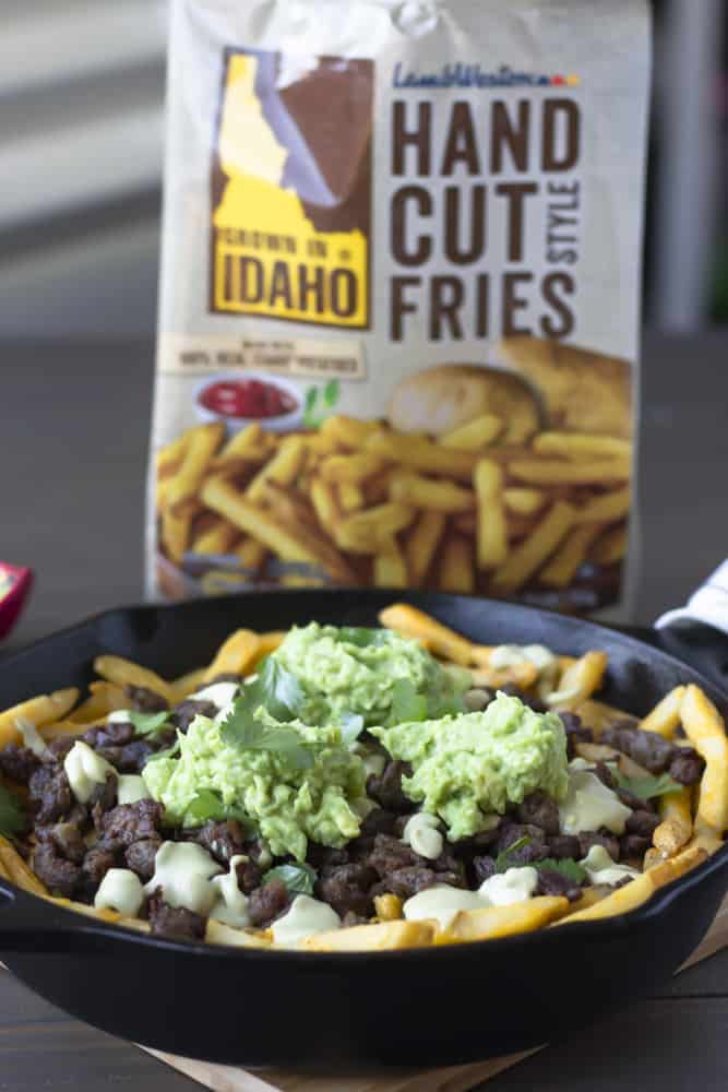 Completed carne asada fries in a skillet with bag of fries in the background.