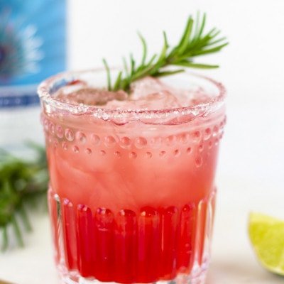 Up close view of elderberry margarita in a clear glass and garnished with a sprig of rosemary.