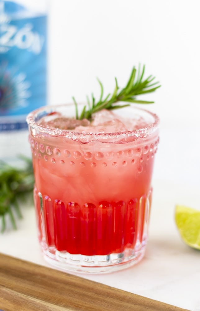 Up close view of elderberry margarita in a clear glass and garnished with a sprig of rosemary.