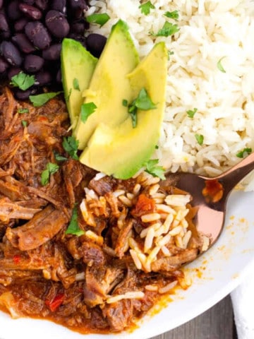 Red shredded beef, white rice, black beans, and sliced avocado on top.