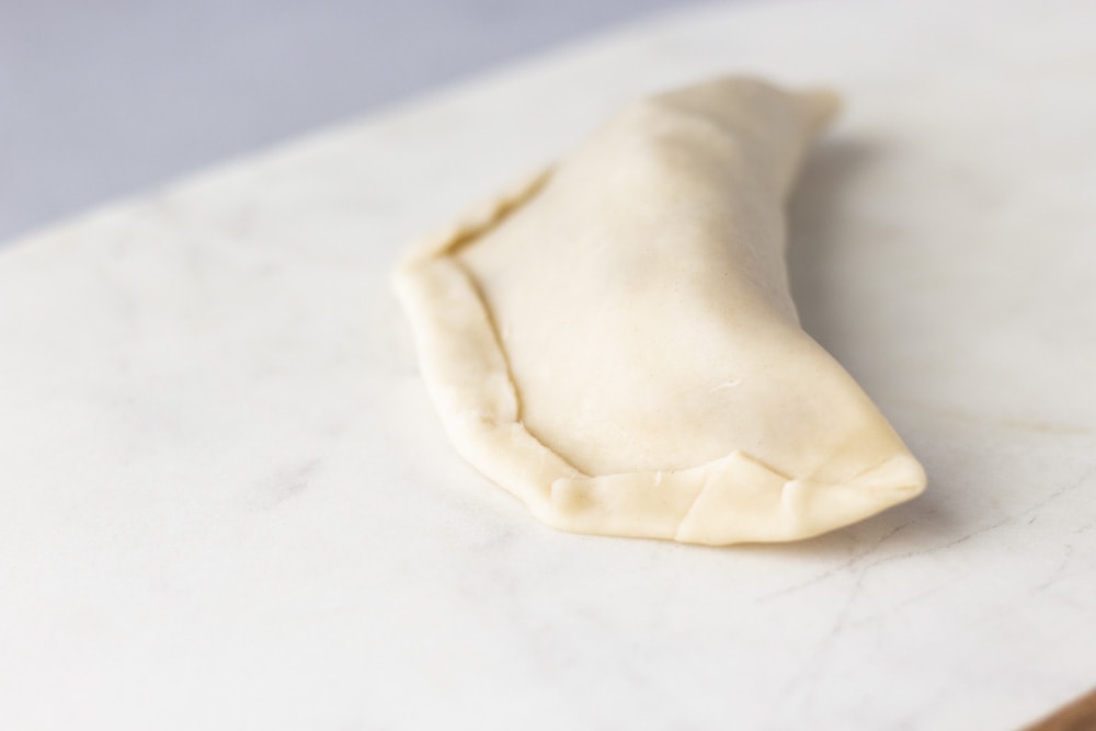 Up close view showing how to fold the edges of the empanada on unbaked dough.