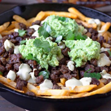 Fries in a cast iron skillet topped with steak, queso, and guacamole.
