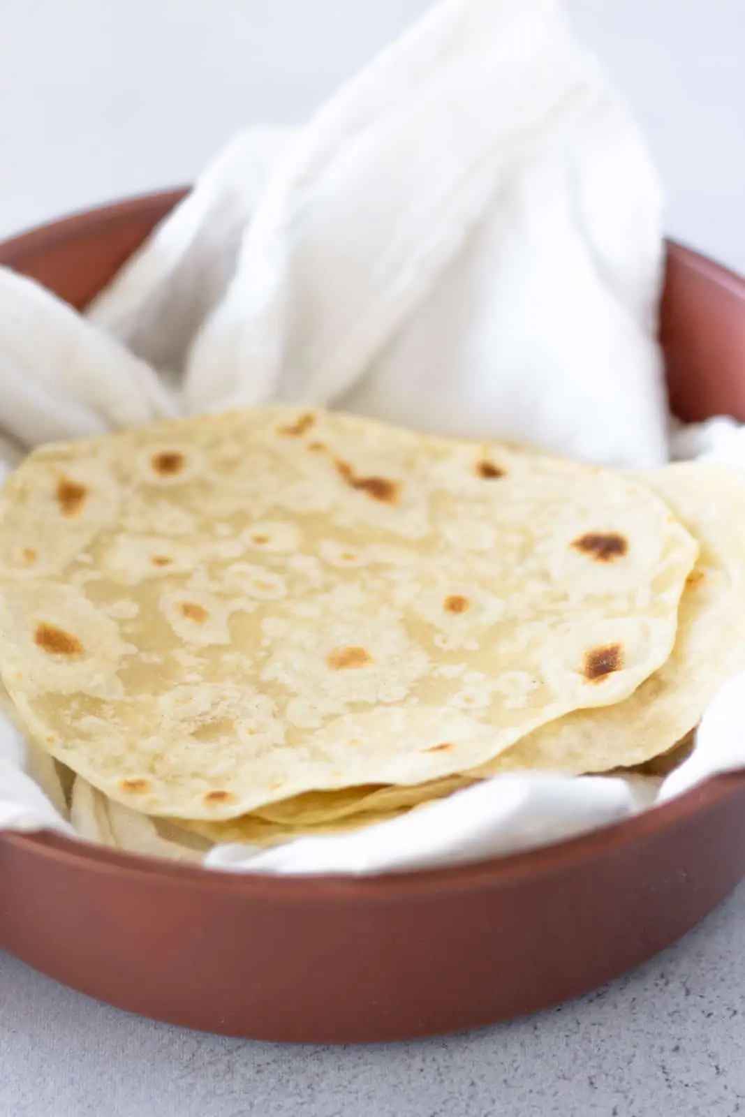 Tortillas stacked in a brown tortilla warmer with a white cloth inside.