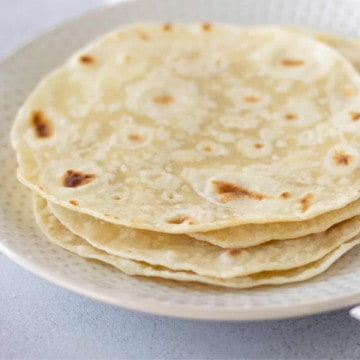 Feature image of flour tortillas stacked on a plate.