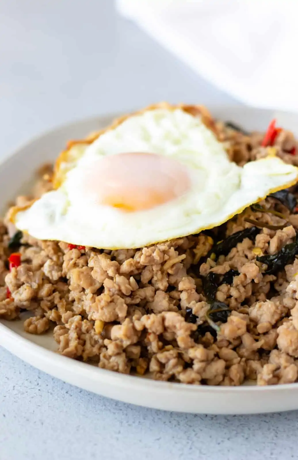 Up close view off pork basil on a white plate and topped with a fried egg.