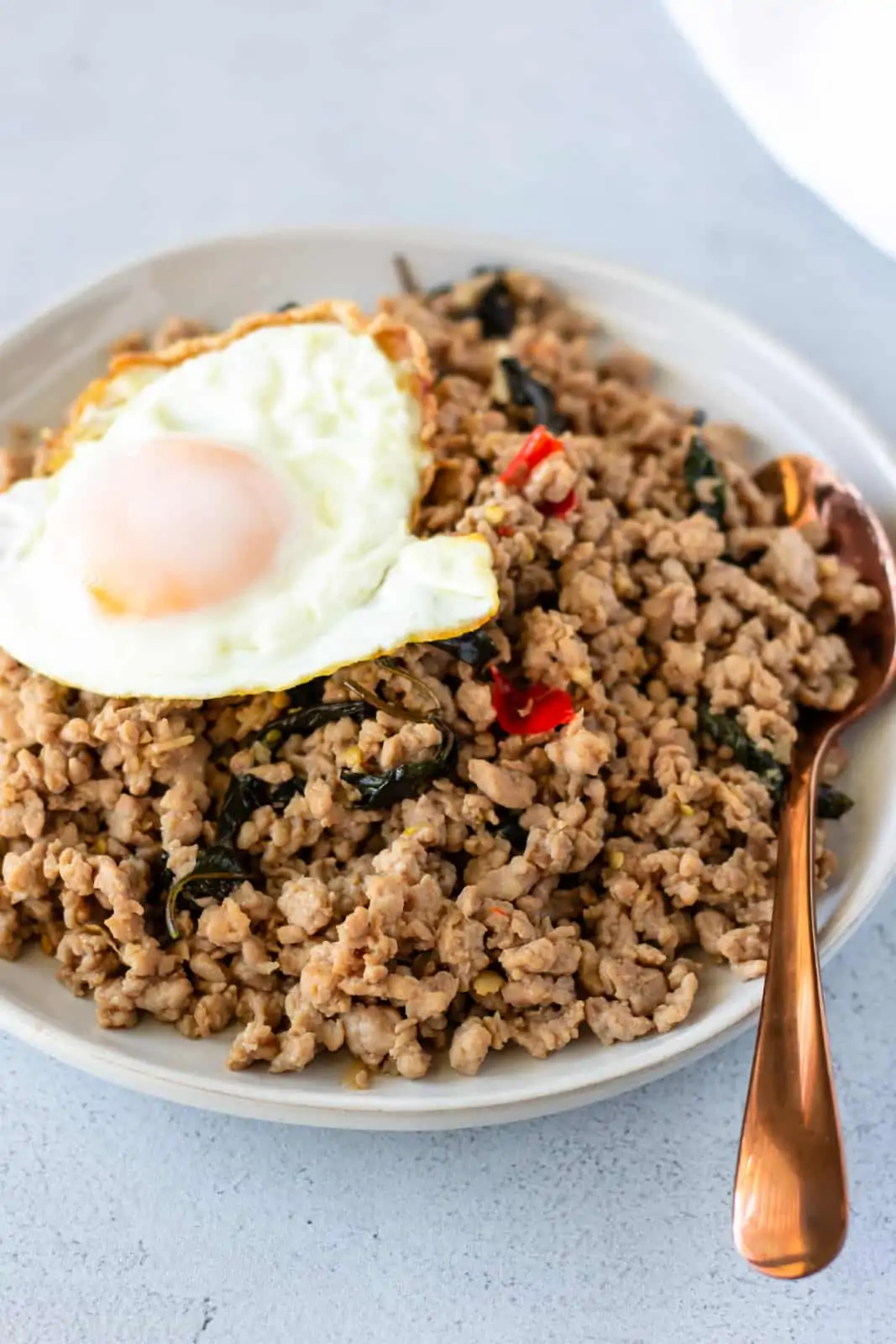 Ground pork stir fry on a white plate topped with a fried egg and bronze color spoon on the side.