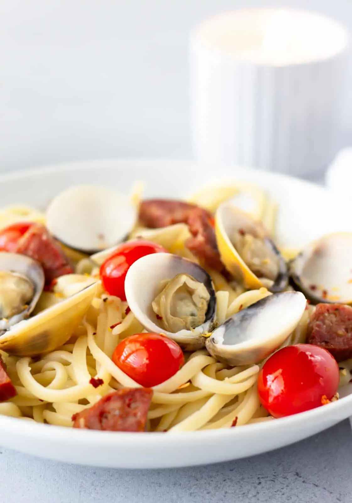 Up close view of pasta in a white dish and a white candle burning in the background