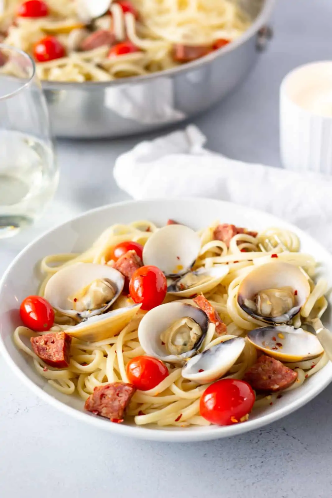 Bowl of pasta with a glass of wine in the background and skillet of pasta in the back.