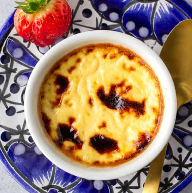 Blue plate with custard in a white ramekin with a strawberry on the side.