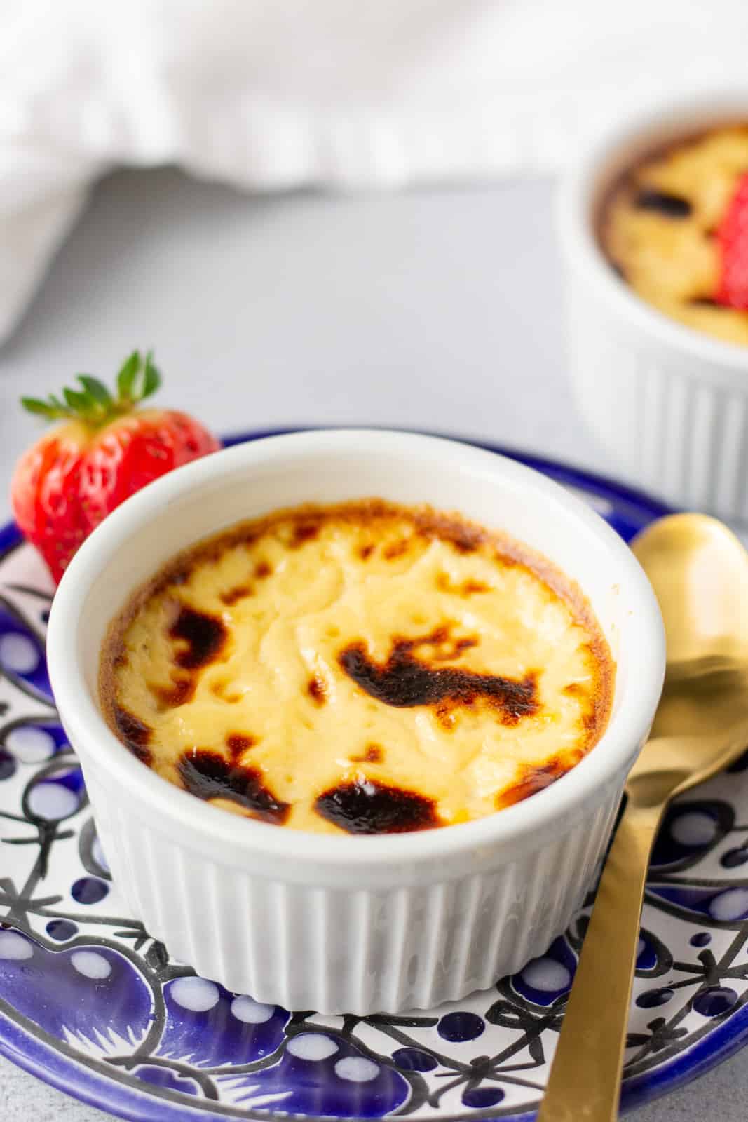 Jericalla in a white ramekin on a blue plate with a gold spoon on the side.